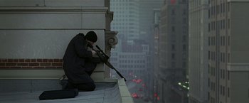 Movie still from “Lucky Number Slevin” (2006), directed by Paul McGuigan – A man with a rifle sitting on the ledge of a building; Wide shot, Low angle