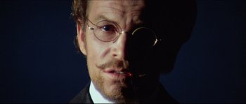 Movie still from “Ludwig” (1973), directed by Luchino Visconti – A person wearing glasses and a suit; Close Up shot, Low angle