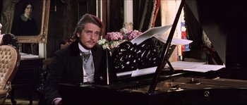 Movie still from “Ludwig” (1973), directed by Luchino Visconti – A man sitting at a piano in front of a bunch of flowers; Medium shot, Over the shoulder angle