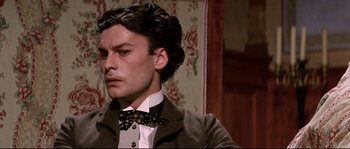 Movie still from “Ludwig” (1973), directed by Luchino Visconti – A man in a suit and bow tie in front of a floral wallpaper; Close Up shot, Low angle