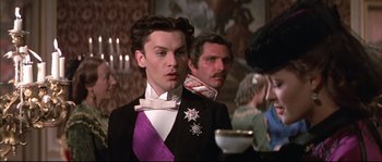 Movie still from “Ludwig” (1973), directed by Luchino Visconti – A man in a suit and a purple bow tie in front of other men; Close Up shot, Low angle