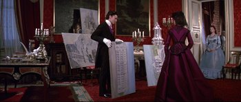 Movie still from “Ludwig” (1973), directed by Luchino Visconti – A man in a suit and gloves holding a painting; Wide shot, Low angle