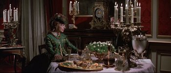 Movie still from “Ludwig” (1973), directed by Luchino Visconti – A woman sitting at a table with a plate of food on top of it; Medium shot, High angle
