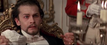 Movie still from “Ludwig” (1973), directed by Luchino Visconti – A person sitting in a chair holding a pen; Close Up shot, Low angle