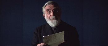 Movie still from “Ludwig” (1973), directed by Luchino Visconti – An old man with a beard and glasses holding a piece of paper in front of him; Close Up shot, Low angle