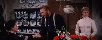 Movie still from “Lust for Life” (1956), directed by George Cukor – A man sitting at a table with a vase of flowers in front of him; Medium shot, Over the shoulder angle