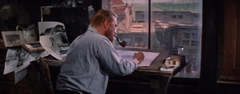 Movie still from “Lust for Life” (1956), directed by George Cukor – A man sitting at a table writing on a piece of paper with a pipe in his mouth; Medium shot, High angle