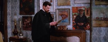 Movie still from “Lust for Life” (1956), directed by George Cukor – A man standing in front of a painting of a person; Medium shot, Low angle
