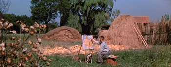 Movie still from “Lust for Life” (1956), directed by George Cukor – A man sitting in the grass painting a picture with a dog nearby; Wide shot, Low angle