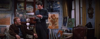 Movie still from “Lust for Life” (1956), directed by George Cukor – A man standing in front of a painting holding a piece of paper in his hands; Medium shot, Over the shoulder angle