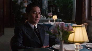 Movie still from “Lust, Caution” (2007), directed by Ang Lee – A man sitting at a table in front of a vase of flowers; Medium shot, Over the shoulder angle