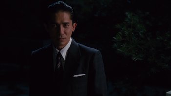 Movie still from “Lust, Caution” (2007), directed by Ang Lee – A man wearing a suit and tie standing in front of a tree; Medium shot, Low angle