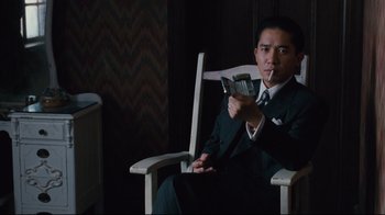 Movie still from “Lust, Caution” (2007), directed by Ang Lee – A man in a suit and tie sitting in a chair holding a cell phone; Medium shot, Low angle