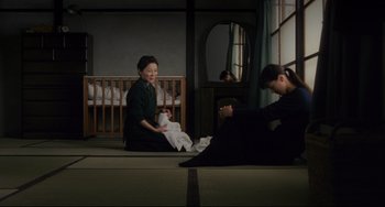 Movie still from “Maborosi” (1995), directed by Kore-eda Hirokazu – A woman sitting on the ground holding a baby; Wide shot, High angle