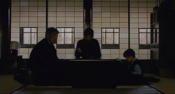 Movie still from “Maborosi” (1995), directed by Kore-eda Hirokazu – Three people sitting at a table with a laptop; Wide shot, Low angle