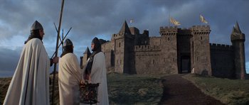Movie still from “Macbeth” (1971), directed by Roman Polanski – Two men in medieval garb standing in front of a castle; Wide shot, Low angle