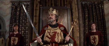 Movie still from “Macbeth” (1971), directed by Roman Polanski – A man dressed as a medieval king holding a sword and holding a staff; Medium shot, Low angle