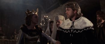 Movie still from “Macbeth” (1971), directed by Roman Polanski – A man and a woman in medieval garb shake hands in front of other people; Medium shot, Over the shoulder angle