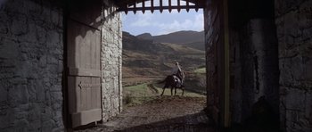 Movie still from “Macbeth” (1971), directed by Roman Polanski – A man riding a horse down a path through a door way; Extreme Wide shot, Low angle