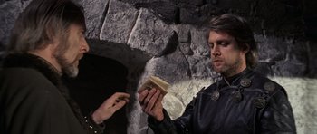 Movie still from “Macbeth” (1971), directed by Roman Polanski – A man holding a book in front of a stone wall; Close Up shot, Over the shoulder angle
