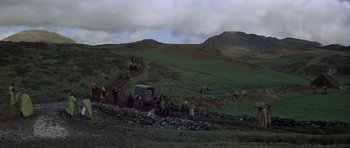 Movie still from “Macbeth” (1971), directed by Roman Polanski – A group of people on a dirt road near a hill; Extreme Wide shot, High angle