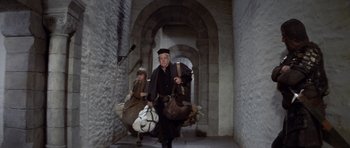 Movie still from “Macbeth” (1971), directed by Roman Polanski – A man and a boy are carrying bags of luggage down a hallway; Wide shot, Low angle