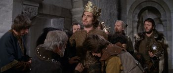 Movie still from “Macbeth” (1971), directed by Roman Polanski – A group of men in medieval garb are gathered around a man wearing a crown; Medium shot, Low angle