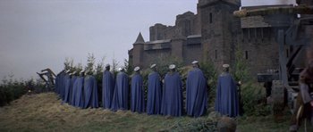 Movie still from “Macbeth” (1971), directed by Roman Polanski – A group of men in blue capes standing next to each other in front of a castle; Extreme Wide shot, High angle