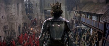 Movie still from “Macbeth” (1971), directed by Roman Polanski – A crowd of people are gathered around a man wearing a suit of armor; Wide shot, High angle