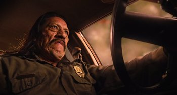 Movie still from “Machete” (2010), directed by Robert Rodriguez – A police officer sitting in the drivers seat of a car; Close Up shot, Low angle