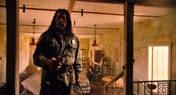 Movie still from “Machete” (2010), directed by Robert Rodriguez – A man with long black hair holding a knife in a room; Medium shot, Over the shoulder angle