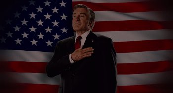 Movie still from “Machete” (2010), directed by Robert Rodriguez – A man in a suit and red neck tie standing in front of an american flag; Medium shot, Low angle