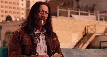 Movie still from “Machete” (2010), directed by Robert Rodriguez – A man with long hair smoking a cigarette outside; Medium shot, Over the shoulder angle