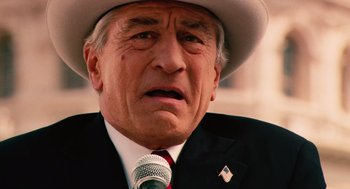 Movie still from “Machete” (2010), directed by Robert Rodriguez – An older man wearing a white cowboy hat and holding a microphone in front of him; Close Up shot, Low angle