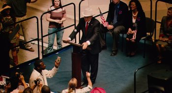 Movie still from “Machete” (2010), directed by Robert Rodriguez – A man in a suit and a white hat speaking to a crowd; Wide shot, High angle