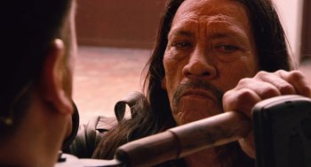 Movie still from “Machete” (2010), directed by Robert Rodriguez – A man with long black hair holding a wooden stick; Close Up shot, Over the shoulder angle
