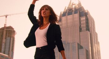 Movie still from “Machete” (2010), directed by Robert Rodriguez – A woman in black jacket and white shirt near a tall building; Medium shot, Low angle