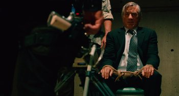Movie still from “Machete” (2010), directed by Robert Rodriguez – A man in a suit and tie sitting in front of a camera; Medium shot, Low angle