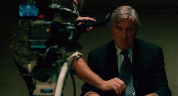 Movie still from “Machete” (2010), directed by Robert Rodriguez – A man in a suit and tie sitting in front of a video camera; Medium shot, Over the shoulder angle