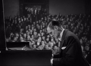 Movie still from “Mad Love” (1935), directed by Karl Freund – A black and white photo of a man playing a piano in front of an audience; Medium shot, High angle
