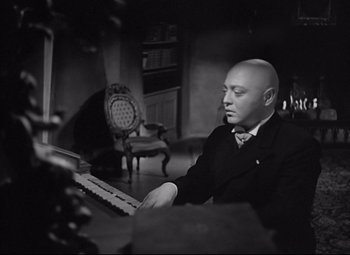 Movie still from “Mad Love” (1935), directed by Karl Freund – A man in a suit and tie sitting in front of a keyboard; Medium shot, Low angle