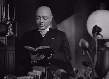 Movie still from “Mad Love” (1935), directed by Karl Freund – A man in a suit and tie reading a book; Medium shot, Low angle
