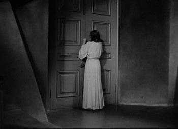 Movie still from “Mad Love” (1935), directed by Karl Freund – A black and white photo of a woman standing in front of a door; Wide shot, High angle