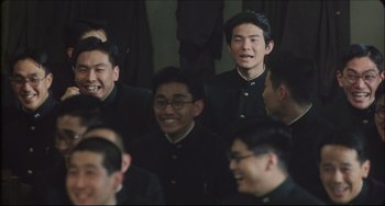 Movie still from “Madadayo” (1993), directed by Akira Kurosawa – A group of men in black suits smiling for the camera; Medium shot, Over the shoulder angle