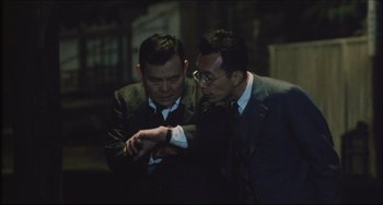Movie still from “Madadayo” (1993), directed by Akira Kurosawa – A couple of men in suits looking at a wrist watch; Medium shot, Over the shoulder angle