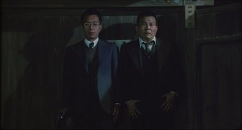 Movie still from “Madadayo” (1993), directed by Akira Kurosawa – Two men in suits and ties standing next to each other; Medium shot, Low angle