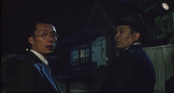 Movie still from “Madadayo” (1993), directed by Akira Kurosawa – Two men standing next to each other in front of a building; Medium shot, Low angle