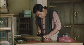 Movie still from “Madadayo” (1993), directed by Akira Kurosawa – A man cutting meat on a wooden cutting board; Medium shot, High angle