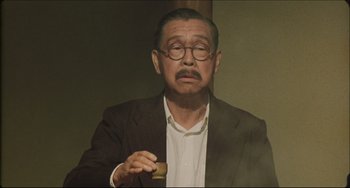 Movie still from “Madadayo” (1993), directed by Akira Kurosawa – An older man in a brown jacket holding a wooden object; Medium shot, Low angle
