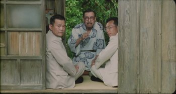 Movie still from “Madadayo” (1993), directed by Akira Kurosawa – A group of three men sitting on top of each other in front of a tree; Medium shot, High angle